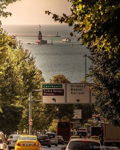 cars are driving on the road near the water and trees in front of some boats