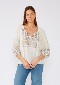 [Color: Natural/Taupe] A front facing image of a brunette model wearing an ivory flowy bohemian peasant top with embroidered detail and tassel ties. Bohemian V-neck Blouse With Embroidered Hem, Beige Linen Tops With Floral Embroidery, Bohemian V-neck Embroidered Top, Traditional Embroidered V-neck Peasant Top, Folk Style V-neck Blouse With Embroidered Neckline, Summer Embroidered V-neck Peasant Top, Spring V-neck Peasant Top, Fall Linen Tops With Floral Embroidery, Spring Folk Style V-neck Peasant Top