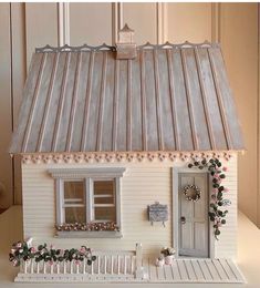 a white doll house with a metal roof and flowers on the windowsill is shown