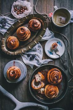 an assortment of pastries in pans on a wooden table next to utensils