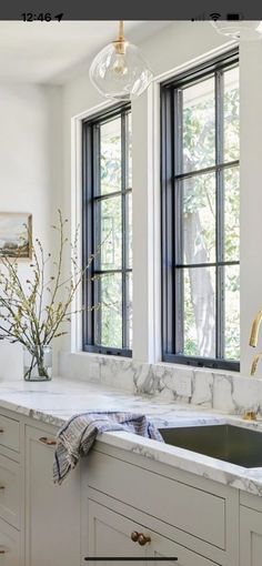 a white kitchen with marble counter tops and gold faucet, two large windows above the sink