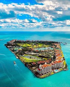 an island in the middle of the ocean with buildings on it and boats sailing by