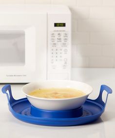 a bowl of soup is sitting on a blue plate in front of a white microwave