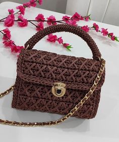 a brown handbag sitting on top of a table next to pink flowers and a gold chain