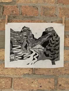 a piece of paper hanging on a brick wall with a drawing of mountains in the background