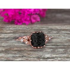 an engagement ring with a black diamond in the center on a wooden table next to pink flowers