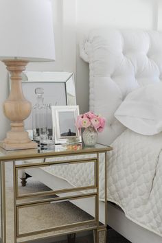 a white bed sitting next to a lamp on top of a table