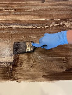 a person in blue gloves is using a paint brush on a piece of wood that has been stained brown