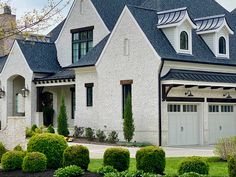 a white brick house with black shingles on the roof and two car garages