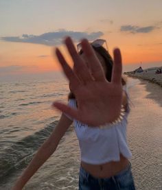 a woman standing on top of a beach next to the ocean holding her hand up