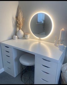 a white vanity with a round mirror and lights on it's sides, next to a stool