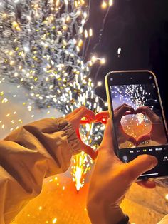 someone taking a photo with their phone of fireworks and heart shaped glasses in front of them