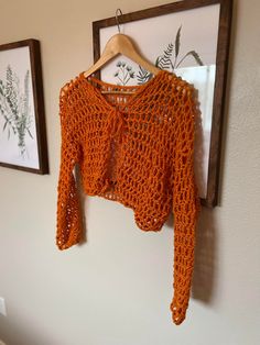 an orange crocheted sweater hangs on a wall next to two framed pictures and a wooden hanger