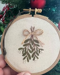 a hand embroidered christmas ornament hanging from a tree with a bow on it