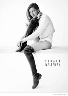 black and white photograph of a woman sitting on a table with her legs crossed, wearing knee high boots