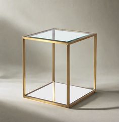 a glass and gold side table on a plain surface with light coming through the top