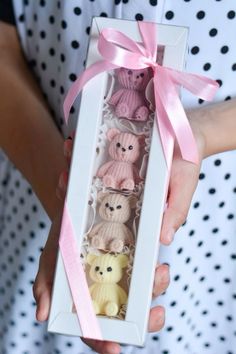 a person holding a box with four small teddy bears in it and a pink ribbon