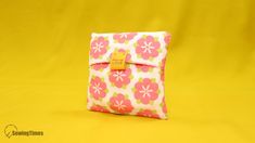 a pink and green flowered pouch with a yellow tag on it sitting on a yellow background