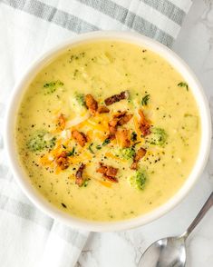 a white bowl filled with broccoli cheese soup on top of a table next to a spoon