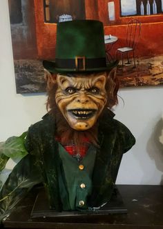 a creepy looking man wearing a green top hat and jacket with his face painted like a demon