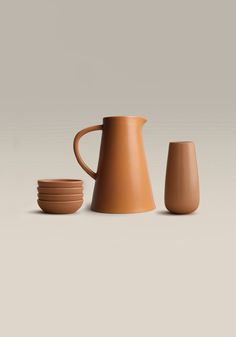 three cups and a pitcher are shown in front of a gray background, one is brown