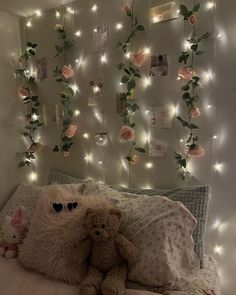 a teddy bear sitting on top of a bed next to a wall covered in lights