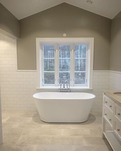 a large white bath tub sitting in a bathroom next to a sink and window with two windows