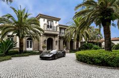 a black sports car parked in front of a large house with palm trees and bushes