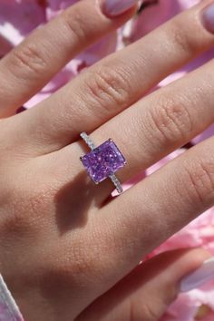 a woman's hand with a ring on it and pink flowers in the background