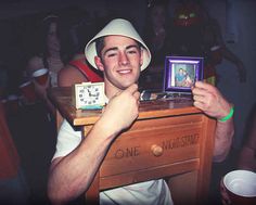 a man in a white hat is holding up a small wooden table with a clock on it