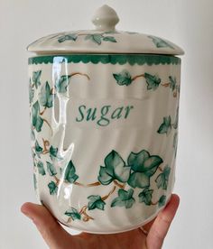 a hand holding a ceramic sugar jar with ivys on it and the word sugar written in cursive writing