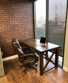 an office desk with a laptop on it in front of a brick wall and window