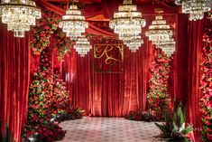 a red and gold wedding setup with chandeliers, flowers, and greenery