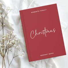 a red christmas memory book next to some baby's breath flowers on a white sheet