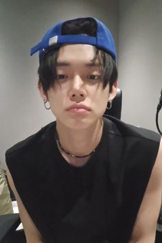 a young man wearing a blue hat sitting in front of a computer desk and looking at the camera