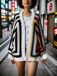 a woman is standing on the sidewalk in shorts and a crocheted sweater with an open front