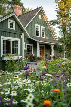 a green house with lots of flowers in the front yard and windows on each side