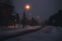 an empty street at night with snow on the ground and street lights in the distance