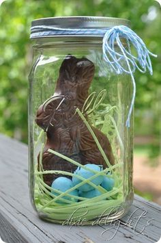 a mason jar filled with blue eggs and a chocolate bunny sitting in the grass next to it