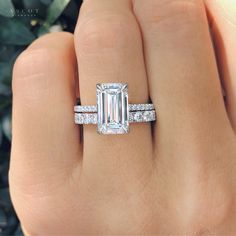 a woman's hand holding an engagement ring with a large emerald stone in the center