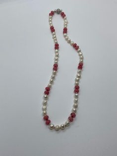 a white and red beaded necklace on a white surface with a silver charm hanging from it's end