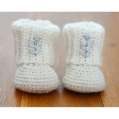 a pair of crocheted white baby boots sitting on top of a wooden floor