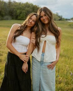 two young women standing next to each other in a field with trees and grass behind them