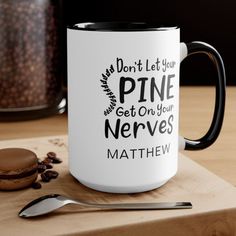 a white and black coffee mug sitting on top of a wooden table next to a cookie