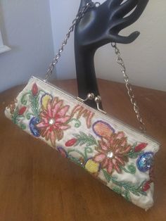 "Vintage beaded floral satin evening clutch. Embroidered, beaded and sequined flowers on white satin. Has a short silver-tone chain which can be tucked inside to use purse as a clutch, has Silver-tone ball latch at top. Inside is in fair vintage condition. Very clean, but there is a 3\" streak of rust stain at the top inside, where metal must have gotten damp and stained the lining. (See photo). Beading and sequins are perfect, no fraying or loose threads despite its 40 plus years!" Multicolor Clutch For Evening In Spring, Spring Evening Clutch Embroidered, Spring Evening Embroidered Clutch, Spring Party Beaded Clutch, Vintage Embroidered Evening Bag For Party, Vintage Embellished Clutch For Party, Vintage White Embellished Evening Bag, Embroidered Clutch For Evening In Summer, Embellished Clutch For Summer Evenings