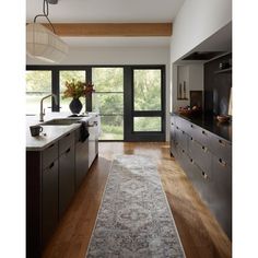 a kitchen with wooden floors and black cabinetry, along with a rug on the floor