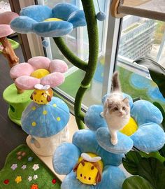 a white cat standing on top of a blue and yellow flower shaped stuffed animal in front of a window