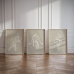 three framed art pieces on the floor in front of a white wall and wooden floors