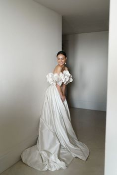 a woman in a white dress is standing by a wall and posing for the camera