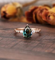 a green and white diamond ring sitting on top of a wooden table next to roses